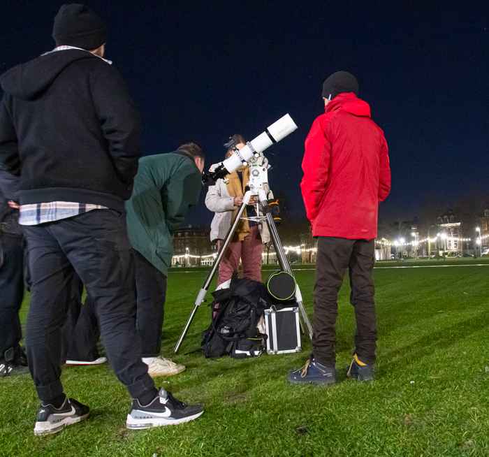 A telescope surrounded by people, one of whom is looking through the telescope