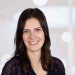 Lecturer Carolin smiling at camera, dark shirt and hair, light background