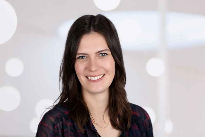 Lecturer Carolin smiling at camera, dark shirt and hair, light background