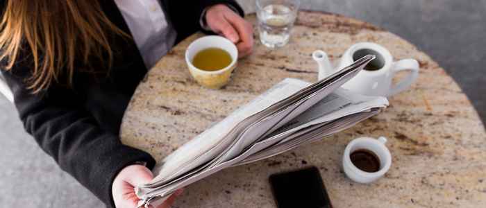 Vrouw leest krant aan tafeltje met koffie